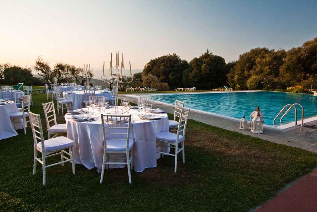 Wedding dinner by the pool with round tables and chandeliers at Tenuta di Artimino